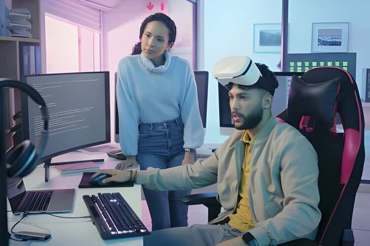 Mulher em pé e homem sentado olhando para a tela de um computador
