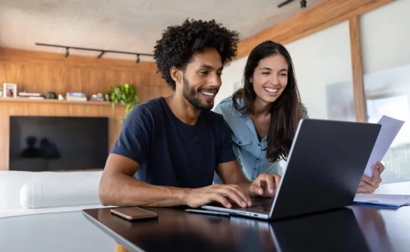 Homem na frente de um latptop e mulher ao lado dele segurando uma folha