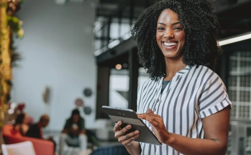 Mulher sorrindo para câmera enquanto segura um tablet