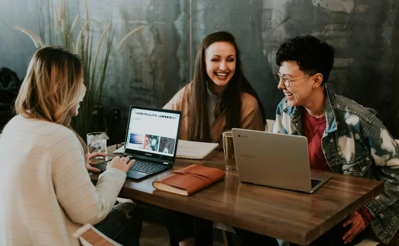 Pessoas ao redor de uma mesa com computadores. Elas estão rindo