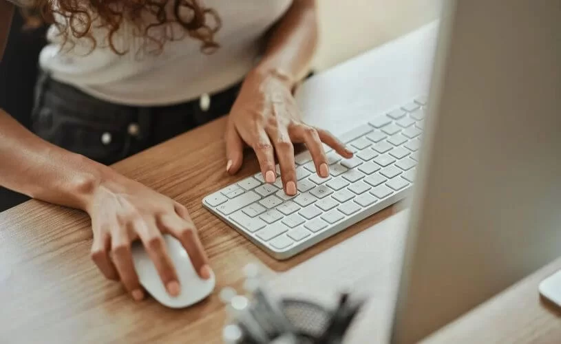 Mulher usando mouse e teclado em um desktop. O rosto dela não aparece
