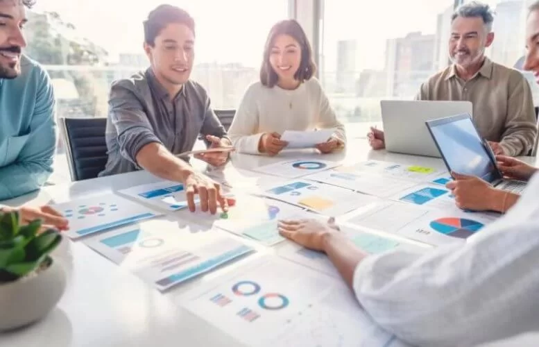 Equipe de trabalho ao redor de mesa com vários gráficos sobre a superfície