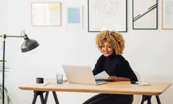 Mulher sorrindo diante de um notebook, em um ambiente minimalista