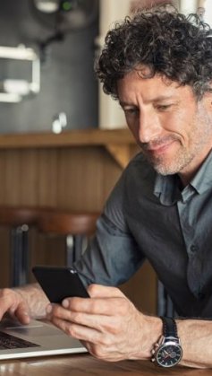 Homem verificando celular e notebook