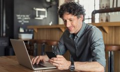 Homem verificando celular e notebook