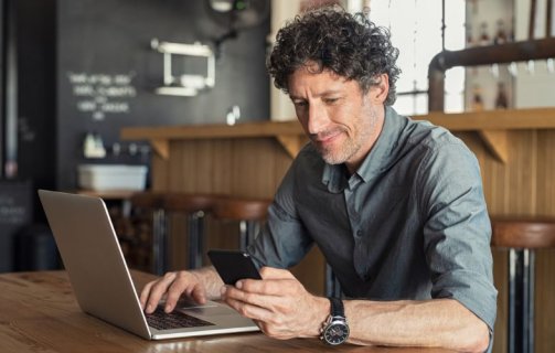 Homem verificando celular e notebook