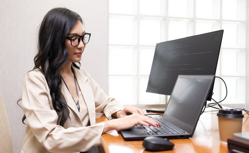Programadora trabalhando com laptop e tela auxiliar