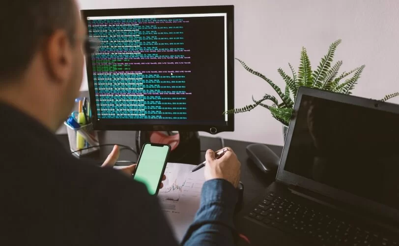 Programador utilizando monitor, smartphone e laptop