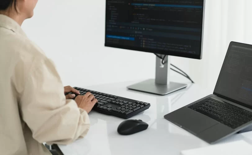 Desenvolvedora programando código em laptop com monitor secundário