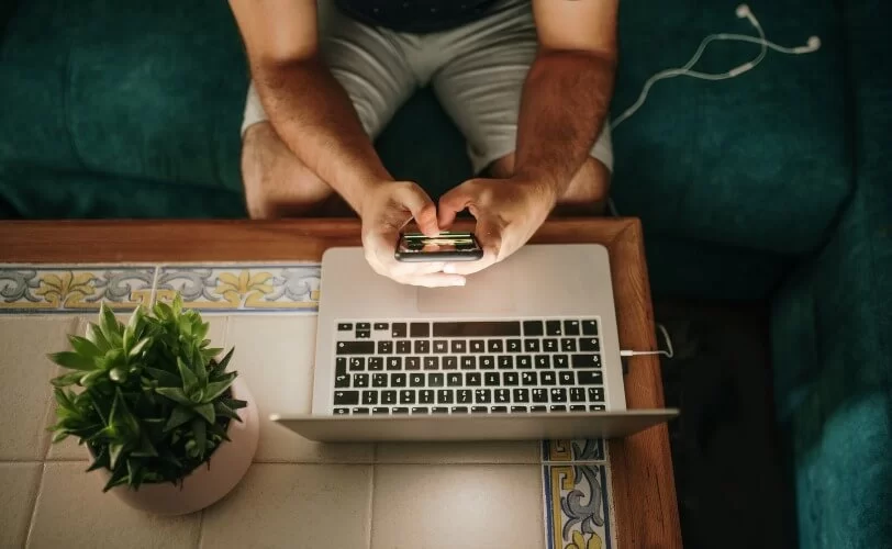 Homem segurando smartphone enquanto trabalha em laptop