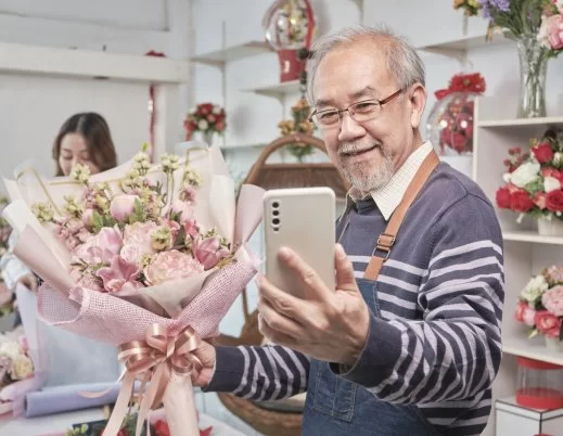 Vendedor asiático fazendo selfie de um buquê de flores em uma loja.