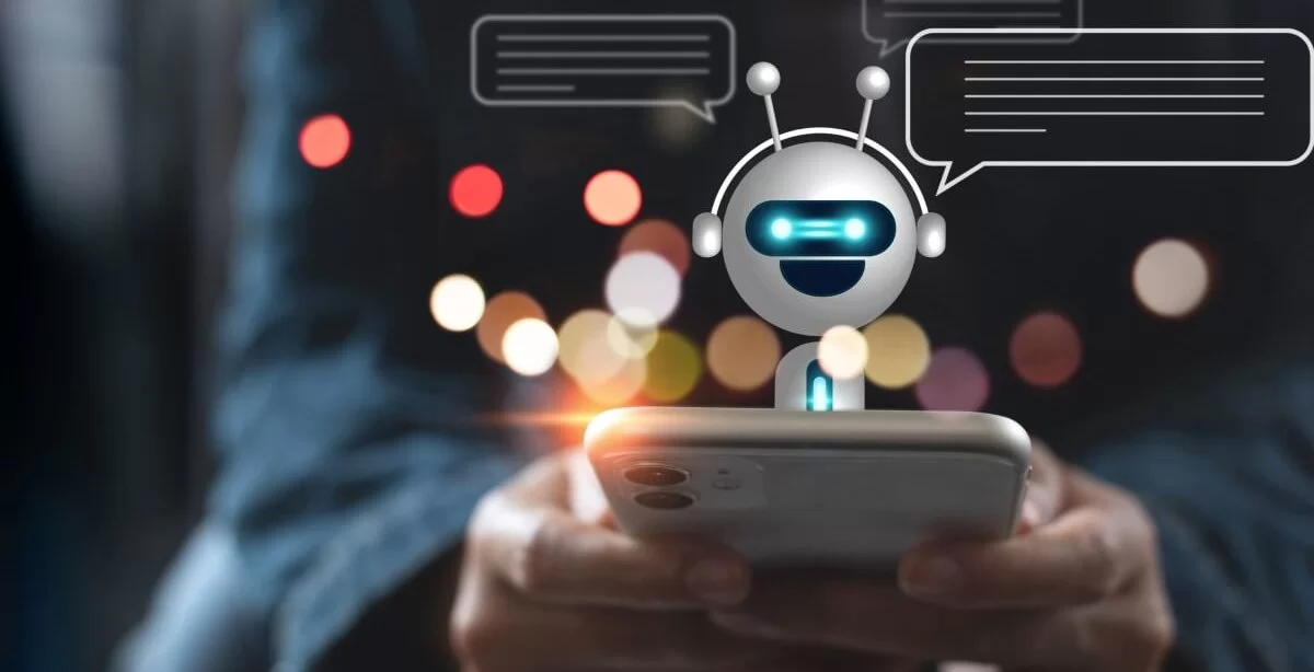 A imagem mostra uma pessoa digitando em um celular para interagir com um robô. Ele aparece saindo da tela, indicando que uma conversa está em andamento.
