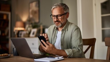 A imagem mostra um homem de meia-idade diante de um notebook e com um celular na mão. Após alguns trabalhos com localhost, ele verifica o funcionamento de uma aplicação no smartphone.