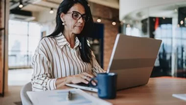 A imagem mostra uma mulher de meia-idade usando roupa social em um escritório. Ela está diante de um notebook, trabalhando na construção de sites e otimizando imagens WebP para deixá-los mais rápidos.
