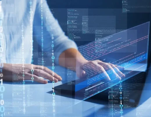 A imagem mostra um homem digitando códigos de programação em um notebook. O rosto dele não aparece. Podemos ver o recurso de IA para programação em ação, já que aparecem vários códigos binários e outros códigos em primeiro plano.