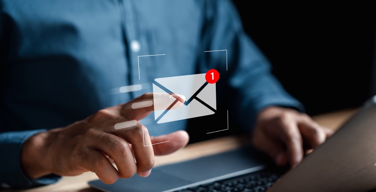 A imagem mostra o funcionário de uma empresa recebendo uma mensagem de e-mail. O rosto dele não aparece. Ele está diante de um notebook e simula tocar na imagem de um envelope branco com o alerta de número 1 para abrir a mensagem que acabou de chegar.