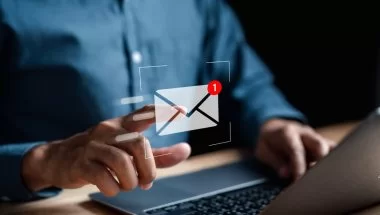 A imagem mostra o funcionário de uma empresa recebendo uma mensagem de e-mail. O rosto dele não aparece. Ele está diante de um notebook e simula tocar na imagem de um envelope branco com o alerta de número 1 para abrir a mensagem que acabou de chegar.