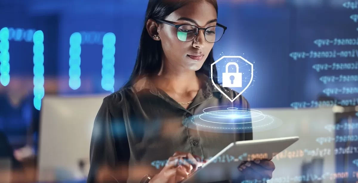 A imagem mostra uma mulher branca de óculos em um escritório digitando em um tablet. Ela está fazendo verificações de segurança para evitar o cross-site scripting (XSS). Há um símbolo de cadeado fazendo referência à segurança acima do dispositivo.