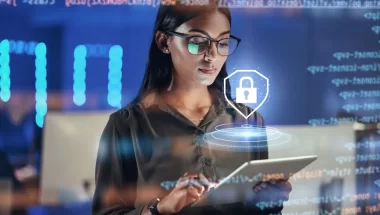 A imagem mostra uma mulher branca de óculos em um escritório digitando em um tablet. Ela está fazendo verificações de segurança para evitar o cross-site scripting (XSS). Há um símbolo de cadeado fazendo referência à segurança acima do dispositivo.