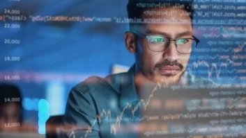 A imagem mostra um homem diante de uma tela com diversas linhas de códigos de programação. Pela quantidade de informações presentes, ele provavelmente está realizando um processo de debug.