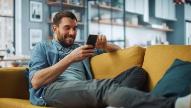 A imagem mostra um homem sorrindo enquanto toca a tela de seu smartphone. Ele possivelmente está em uma rede social e foi impactado pela publicação de uma empresa, que sabe quais são os melhores horários para postar no TikTok.