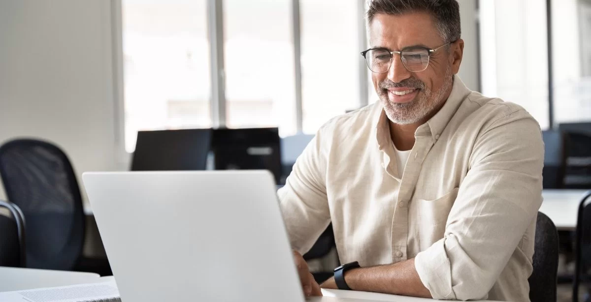A imagem mostra um homem de meia-idade em um escritório digitando em um notebook. Ele possivelmente está analisando um slug que foi criado para a publicação de um post em seu blog.