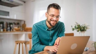 A imagem mostra um homem trabalhando em um notebook. Ele está no que parece ser a cozinha de um escritório e, possivelmente, está realizando uma busca para saber como descobrir a fonte de uma imagem na internet.