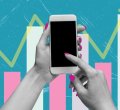 Um par de mãos femininas desliza um dos dedos indicadores sobre a tela do celular. Ao fundo, é possível visualizar barras brancas e rosas, que compõe um gráfico disposto sob as mãos, representando a ideia em torno das principais tendências de marketing para 2025.