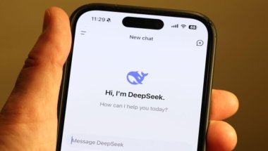 Imagem mostra um smartphone exibindo o logotipo do "DeepSeek", sendo segurado por uma mão de uma pessoa branca. O design sugere uma identidade visual moderna e tecnológica, relacionada a uma ferramenta de inteligência artificial.