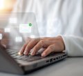 Uma pessoa branca, usando camisa azul claro e gravata cinza, digita em um notebook. Sobre a fotografia, surgem ícones representando e-mails que se conectam entre si.