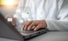 Uma pessoa branca, usando camisa azul claro e gravata cinza, digita em um notebook. Sobre a fotografia, surgem ícones representando e-mails que se conectam entre si.