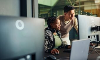 Dois desenvolvedores, homem e mulher, analisando código em um monitor em ambiente de trabalho escuro