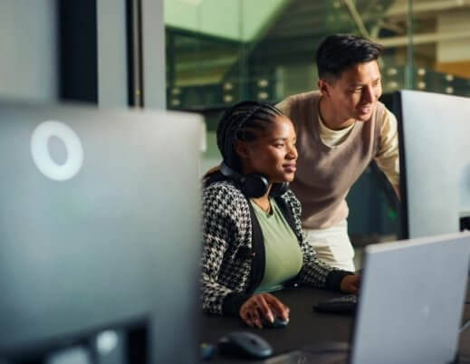 Dois desenvolvedores, homem e mulher, analisando código em um monitor em ambiente de trabalho escuro