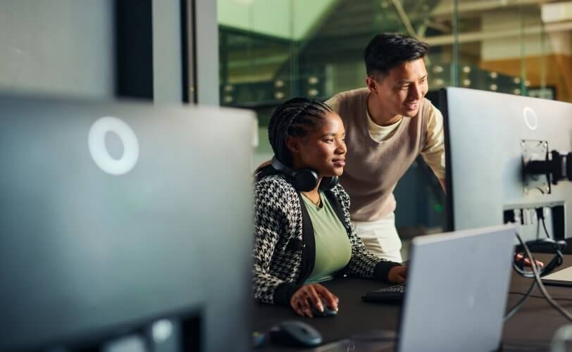 Dois desenvolvedores, homem e mulher, analisando código em um monitor em ambiente de trabalho escuro