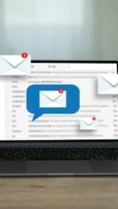 Notebook sobre mesa exibindo caixa de entrada de e-mails, com ícones de mensagens novas surgindo na tela, simbolizando comunicação empresarial e uso de e-mail profissional.
