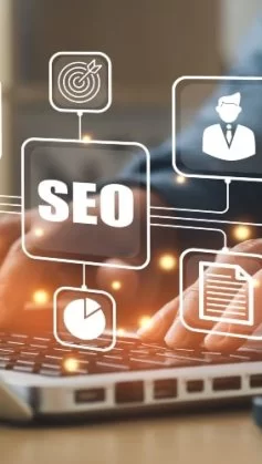 Pessoa digitando em um notebook com ícones digitais flutuantes relacionados a SEO, como gráfico de crescimento, alvo, perfil de usuário, lâmpada de ideia e cifrão, representando estratégias de otimização para mecanismos de busca e performance online.