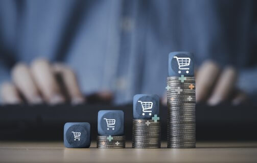 Carrinho de compras empilhado no topo do empilhamento de moedas crescentes para o conceito de crescimento de negócios de venda online.