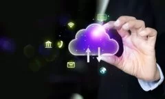 A imagem apresenta um ícone de nuvem digital com setas de upload e download, simbolizando o armazenamento e compartilhamento de informações em sistemas de computação em nuvem. As linhas luminosas e o fundo azul com partículas tecnológicas reforçam a ideia de fluxo de dados, conectividade e infraestrutura digital. Essa representação ilustra como a nuvem (cloud computing) permite o acesso remoto, a integração entre dispositivos e a agilidade nos processos corporativos, sendo um pilar essencial da transformação digital e da inovação tecnológica.