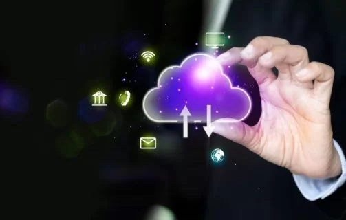 A imagem apresenta um ícone de nuvem digital com setas de upload e download, simbolizando o armazenamento e compartilhamento de informações em sistemas de computação em nuvem. As linhas luminosas e o fundo azul com partículas tecnológicas reforçam a ideia de fluxo de dados, conectividade e infraestrutura digital. Essa representação ilustra como a nuvem (cloud computing) permite o acesso remoto, a integração entre dispositivos e a agilidade nos processos corporativos, sendo um pilar essencial da transformação digital e da inovação tecnológica.