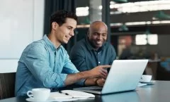 A imagem mostra dois homens conversando em um escritório, enquanto olham para um notebook e discutem sobre criar site com IA.