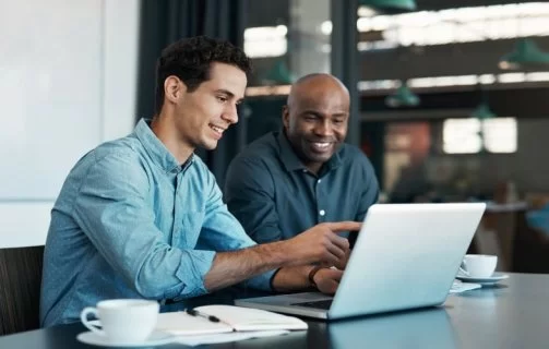 A imagem mostra dois homens conversando em um escritório, enquanto olham para um notebook e discutem sobre criar site com IA.