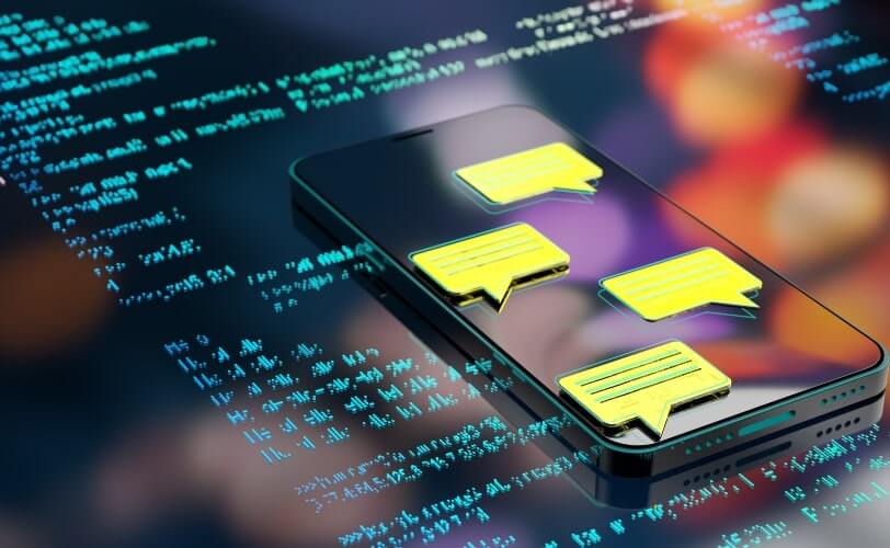A imagem exibe balões de conversa translúcidos e coloridos, flutuando sobre um fundo com linhas de código em linguagem de programação. Um dos balões contém a sigla “AI”, destacando a presença de inteligência artificial e processamento automatizado de linguagem. As cores em degradê neon — mesclando tons de rosa, roxo, laranja e azul — criam um efeito futurista e digital. O cenário representa a integração entre IA e desenvolvimento de software, simbolizando chatbots, assistentes virtuais e sistemas baseados em aprendizado de máquina. É uma composição que transmite inovação, tecnologia e a fusão entre comunicação e automação.